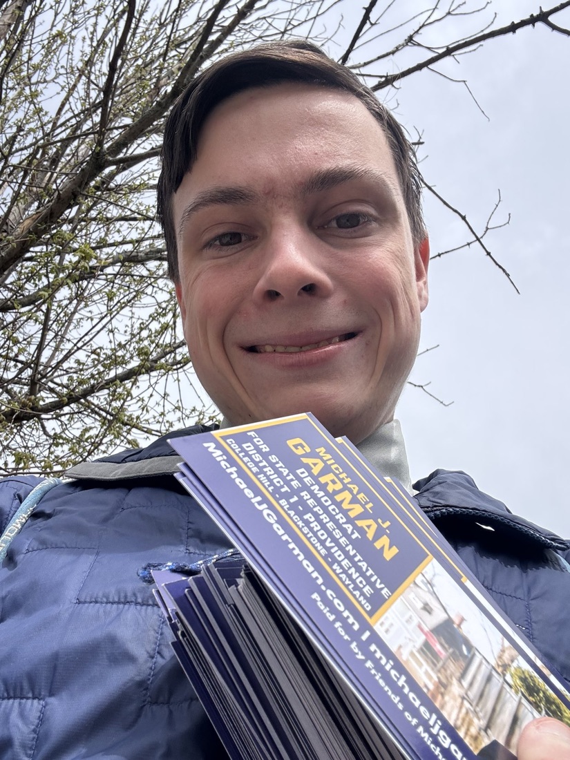 Michael smiling on a canvassing shift, holding a stack of blue-and-gold campaign cards