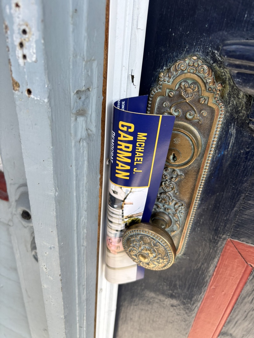 A Garman campaign card tucked behind the ornate brass door handle of an East Side home